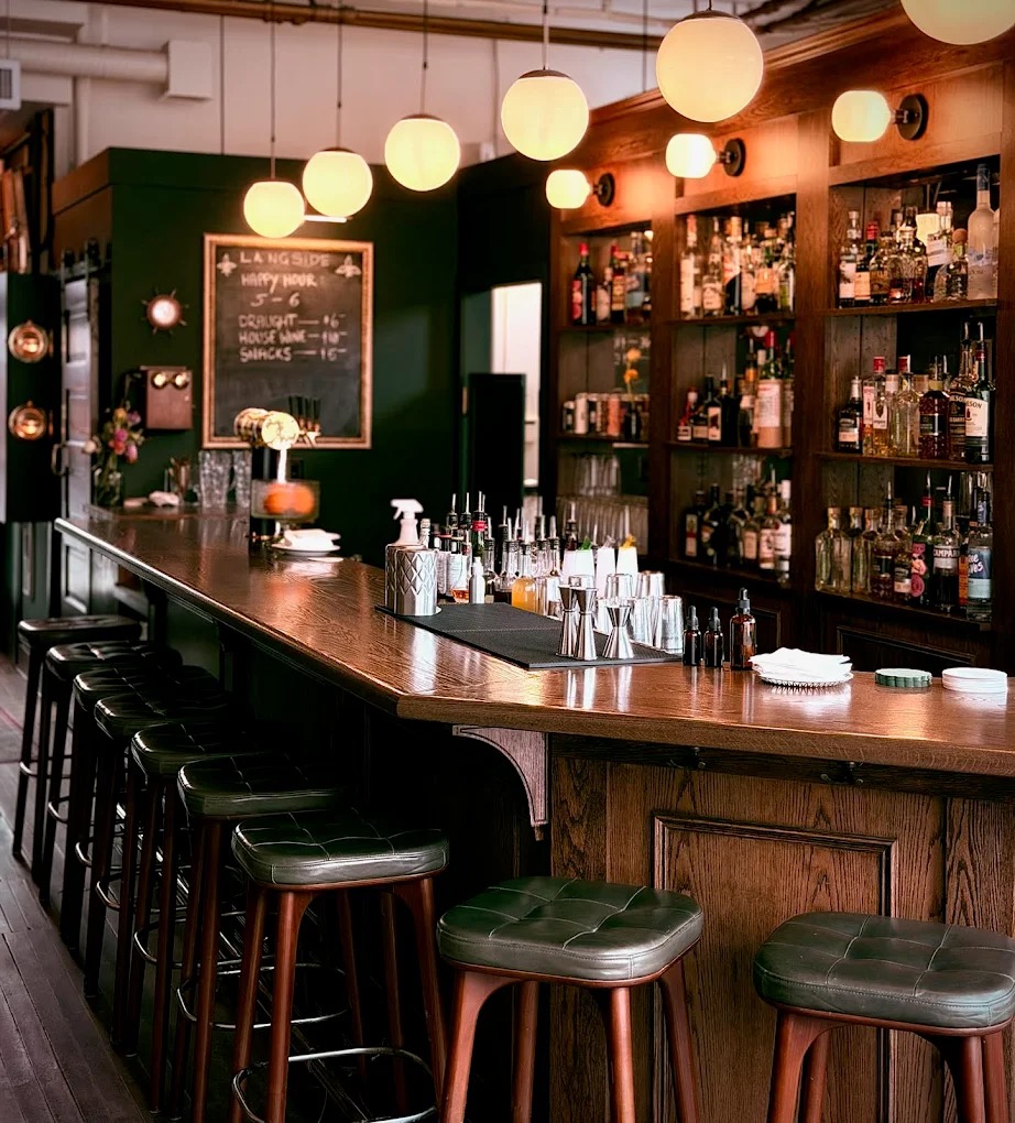 Langside Grocery cocktail bar interior: dark wood bar, green leather stools, and back bar at 164 Langside Street, Winnipeg